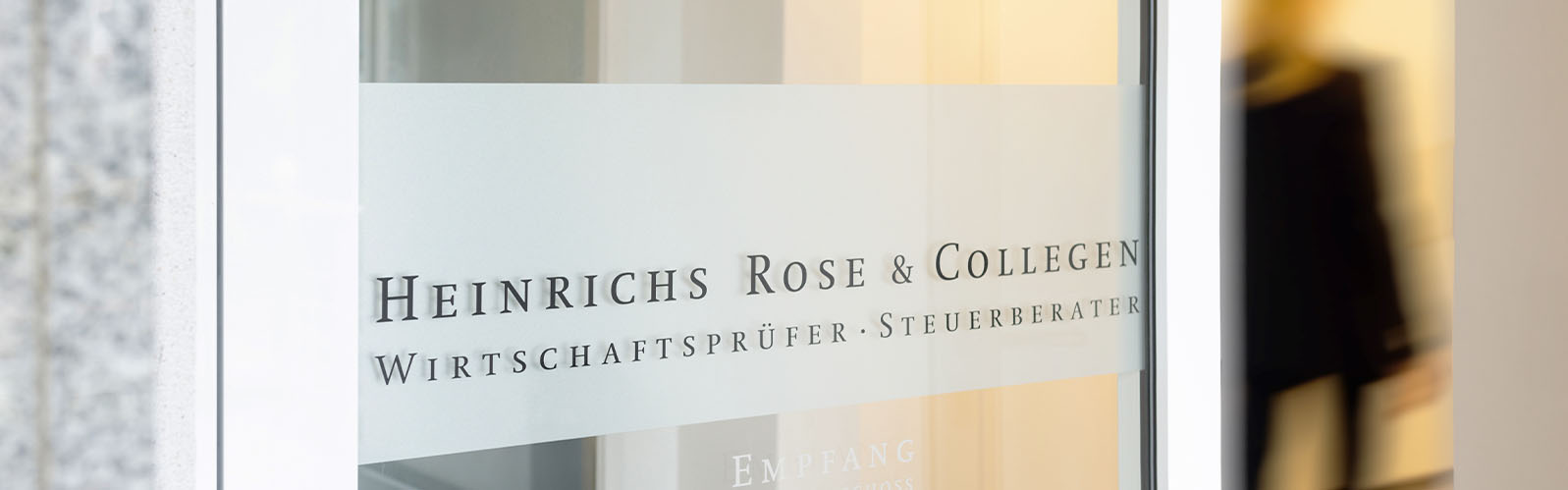 Bildausschnitt Eingangstüre mit Firmenlogo und Person im Flur dahinter mit Bewegungsunschärfe