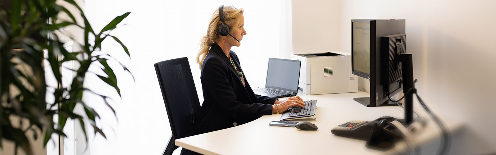 Seitenansicht Frau mit Headset sitzt am Bildschirmarbeitsplatz und tippt auf Tastatur